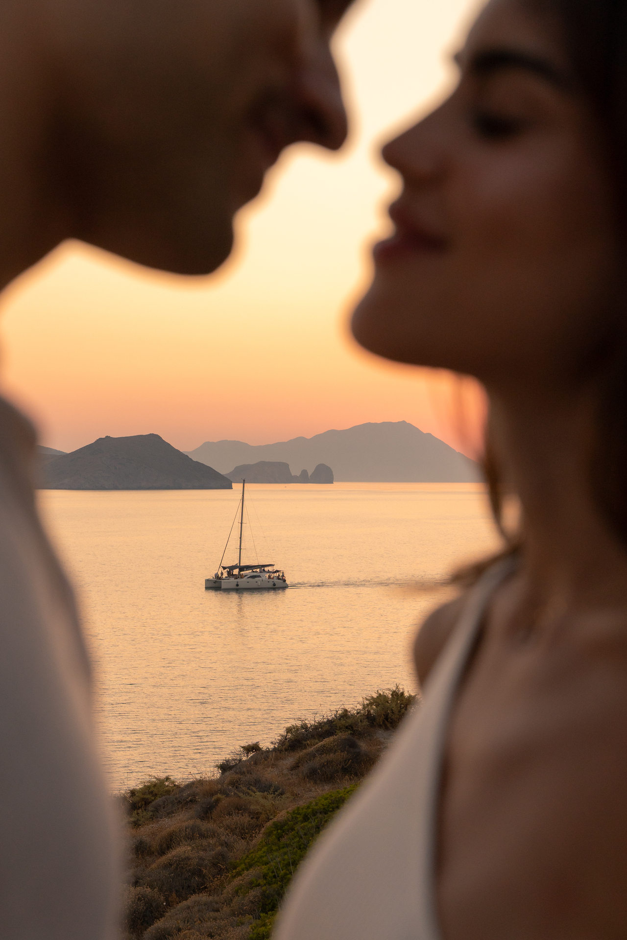 Bride standing on volcanic rock overlooking turquoise Aegean waters
